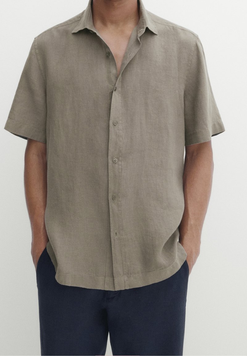 Beige linnen shirt met korte mouwen, een kraag, knopen aan de voorkant en een losse pasvorm, gecombineerd met donkerblauwe broek. Glad in structuur en een minimalistisch ontwerp.