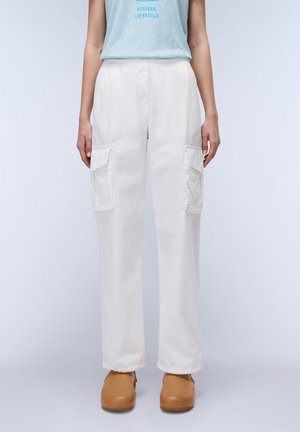 Pantalones cargo blancos con cintura elástica, con bolsillos laterales y un corte holgado. Textura suave, combinados con zapatos marrones de tipo slip-on.