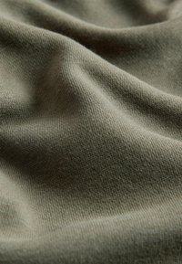 Olivgrüner Strickstoff mit weicher, strukturierter Oberfläche, die ein glattes und leicht dehnbares Aussehen aufweist, sanft in Falten drapiert.
