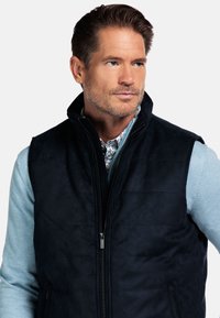 Marineblaue Weste aus weichem, wildlederähnlichem Material mit hohem Kragen, Reißverschluss und seitlichen Taschen mit glatter Textur.