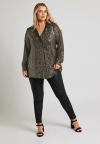 Puku glitterin tumman kultaisena mustalla kauluksella, yhdistettynä mustiin istuviin housuihin ja nauhaketjuihin mustiin korkokenkiin. Kiiltävä pinta ja rento istuvuus.