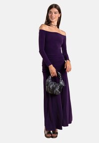 Robe violette à épaules dénudées avec des détails froncés, manches longues et un design fluide. Portée avec un sac à main noir texturé et des chaussures à plateforme.