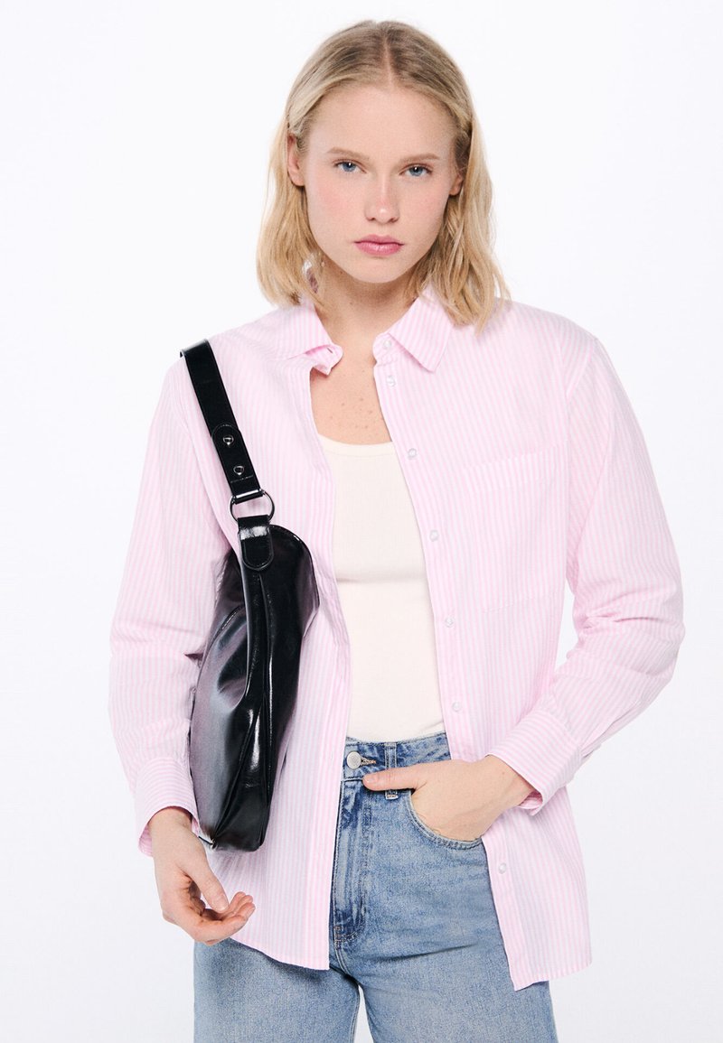 Pink-striped button-up shirt with a pocket, worn over a cream tank top, paired with light blue jeans and a black bag slung over the shoulder.