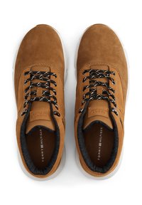 Une paire de sneakers en suède brun à lacets, avec des lacets à motifs noir et blanc et des semelles blanches, vue de dessus sur un fond blanc.