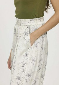 Pantalons imprimés floraux avec une taille élastique, poches latérales, tissu léger, présentant un fond crème et des motifs floraux en art linéaire noir.