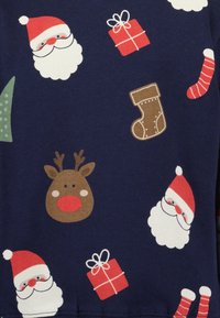 Námorní tkanina s opakujícími se vánočními motivy: obličeje Santa Clause, hlava soba, vánoční punčochy, dárky a vánoční stromy v červené a zelené.