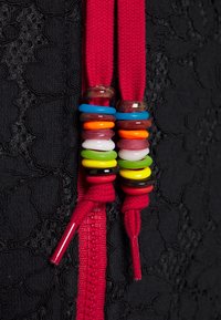 Eindjes van rode schoenveters met gestapelde kleurrijke plastic ringen tegen een getextureerde zwarte stof en een rode rits.