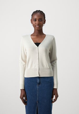 Light beige cardigan with a V-neck and button-down front. Soft texture, long sleeves, and subtle ribbed detailing at the hem. Paired with a denim skirt.