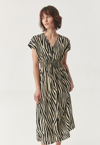 Haljina sa uzorkom zebra, v-izrezom, kratkim rukavima, elastičnim pojasom i dužinom do koljena. Izrađena od lagane tkanine u bež i crnoj boji.
