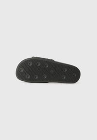 Black shoe sole with a textured surface, featuring circular grip patterns and small raised dots for traction. Flat design with rounded edges.