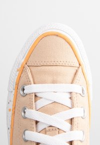 Baskets en toile beige avec semelle en caoutchouc blanche, dotées d'accents orange, de lacets blancs et d'œillets métalliques pour le réglage des lacets.