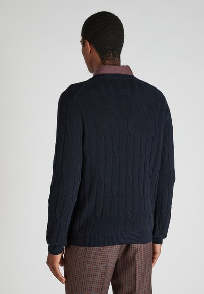 Marineblaue Aran-Strickpullover mit geripptem Saum und Bündchen, ausgestattet mit einem Rundhalsausschnitt. Glatte Textur, sichtbares Strickmuster und weicher Stoff.