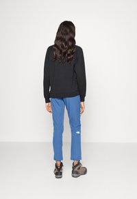 Musta collegepaita, siniset housut ja ruskeat retkeilykengät. Collegepaidassa on joustavat hihansuut ja helma. Housuissa on logo ja säädettävä helma.