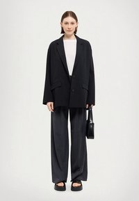 Czarna, oversizeowa marynarka na dwa guziki, zestawiona z szarymi spodniami o szerokich nogawkach. Dopełnieniem stroju są czarna torebka i sandały na platformie. Tkanina z mieszanki bawełny.