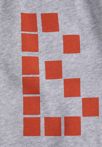 Carrés rouges disposés en un motif évoquant la lettre « B » sur un fond de tissu gris clair texturé.