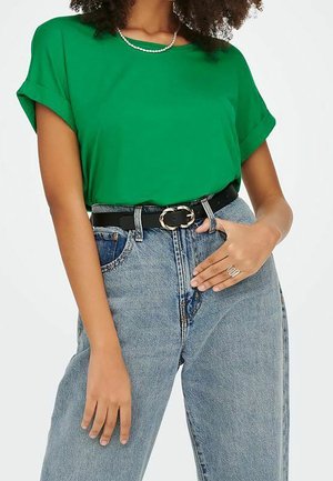 Groen shirt met korte mouwen, gecombineerd met een blauwe high-waisted spijkerbroek en een zwarte riem met een ronde zilveren gesp. Eenvoudige zilveren ring als accent.
