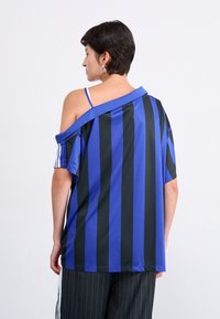 Camisa de rayas azul y negra de gran tamaño con diseño de hombros descubiertos, mangas cortas y un material suave y elástico. Presenta rayas horizontales.
