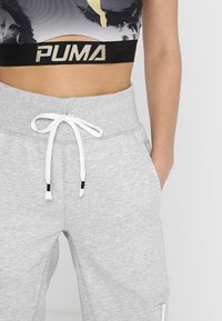 Grijze sweatpants met een tailleband met trekkoord, voorzien van zwart-witte accenten en zijzakken. De tailleband toont een logo in goud.