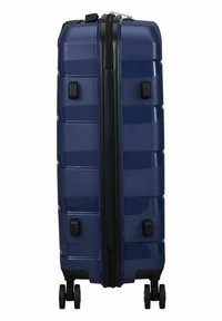 Hard-shell suitcase in dark navy, featuring a textured surface, sturdy zippers, four wheels, and side handles for easy mobility.