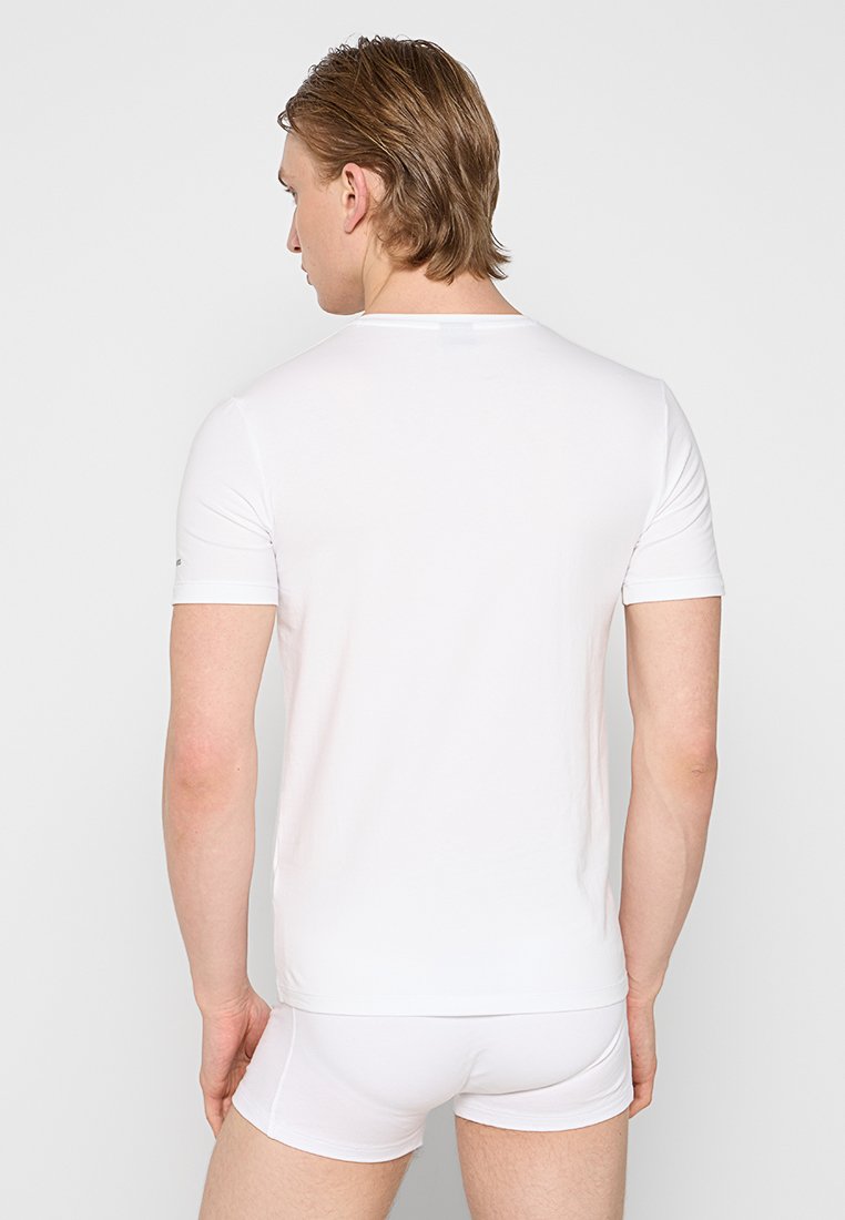 T-shirt blanc à manches courtes en tissu doux, avec un col rond et un design minimaliste, vu de l'arrière contre un fond uni.