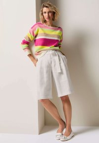Gestreepte gebreide sweater in roze, geel en beige, gecombineerd met hoge witte linnen shorts. Eenvoudige ballet flats met strikdetail.