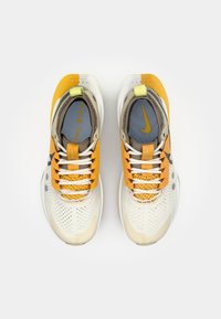 Nike sneakers met een beige en lichtgrijze bovenkant, oranje accenten en een gestructureerd ontwerp, met witte veters en gevoerde binnenzijden.