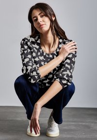 Blusa a righe bianco e nero con maniche a sbuffo, scollatura rotonda e pieghe sottili. Abbinata a jeans scuri e sneakers bianche.