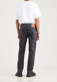 Pantalones vaqueros de mezclilla negra con un diseño de pierna recta, bolsillos traseros visibles y una etiqueta de parche en la cinturilla. Combinados con una camiseta blanca.