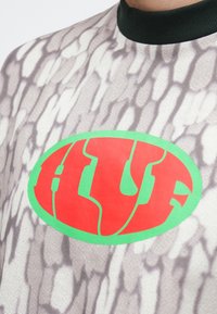 Tričko s krátkym rukávom s textúrovaným vzorom v šedej a bielej farbe, s veľkým červeno-zeleným oválnym logom "HLF" v strede.