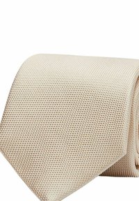 Beige strukturerat slips med ett vävt mönster, med en bred ände och en slät yta, hoprullad för display.