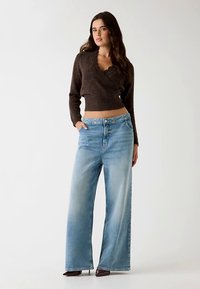 Brown cropped wrap sweater with a textured finish paired with light blue wide-leg jeans, featuring a faded look and front pockets.