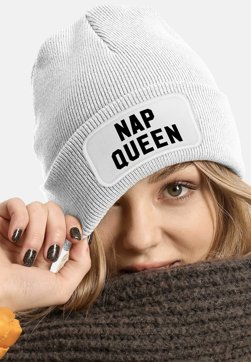 White ribbed beanie featuring a rectangular patch with bold black text "NAP QUEEN." Material appears soft with a snug fit.