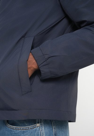 Ναυτικό ελαφρύ μπουφάν με απαλή υφή, ελαστικούς γαντζόδες και πλαϊνές τσέπες. Διαθέτει απλό σχέδιο και ίσια στρίφωμα.