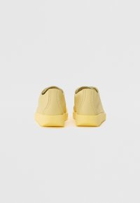 Adidași galbeni cu un finisaj neted și mat. Designul tip slip-on dispune de o talpă din cauciuc și detalii de cusătură pe spate și pe laturi.