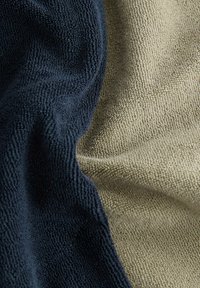 Serviettes en bleu marine et beige clair, avec une surface texturée et un tissu doux, disposées en plis mettant en valeur distinctement les deux couleurs.