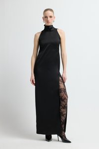 Czarna satynowa sukienka na szyję z wysokim rozcięciem, odsłaniająca przezroczyste czarne koronkowe rajstopy, zestawiona z czarnymi szpilkami. Gładka faktura, dopasowany fason.