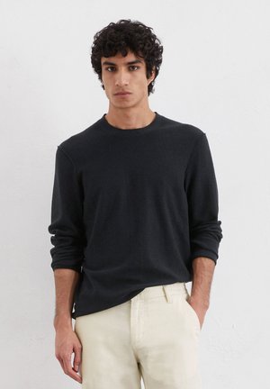 Schwarzes Langarmshirt mit Rundhalsausschnitt, aus einem weichen Material gefertigt, mit einem lässigen Schnitt und gerippten Bündchen, kombiniert mit hellen Hosen.