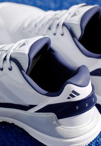 Bílé a námořnické atleticé boty s texturovaným síťovinovým svrškem, polstrovaným límcem a gumovou podrážkou. Funkce značkování na patě a bočních akcentu.