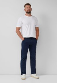 Witte katoenen t-shirt met korte mouwen, gecombineerd met marineblauwe katoenen broeken en witte sneakers. Eenvoudig, op maat gemaakt ontwerp, zonder zichtbare patronen.