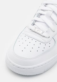 Hvit lær sneakers med perforert tåboks, flate lisser, og sølv "AF1"-tag på tungen, med teksturert gummisåle og sømdetaljer.