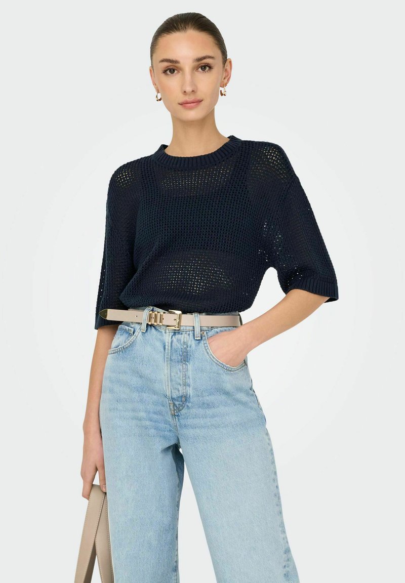 Maglione lavorato a maglia blu navy con maniche corte, caratterizzato da un design a tessitura aperta, abbinato a jeans azzurri a vita alta e una cintura beige.