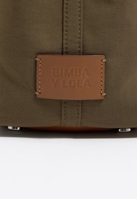 Oliwkowa torba materiałowa z brązową skórzaną metką z wytłoczonym napisem "Bimba y Lola". Posiada obszycia wzdłuż brzegów oraz metaliczne akcenty.