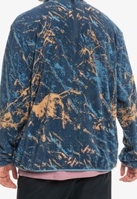 Sudadera de forro polar en un patrón abstracto azul y naranja, con manga larga, cuello alto y un corte relajado con tejido texturizado.