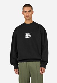 Czarna bluza z okrągłym dekoltem, wykonana z bawełny, z białym graficznym logo na piersi. Posiada luźne rękawy i ściągacz u dołu.