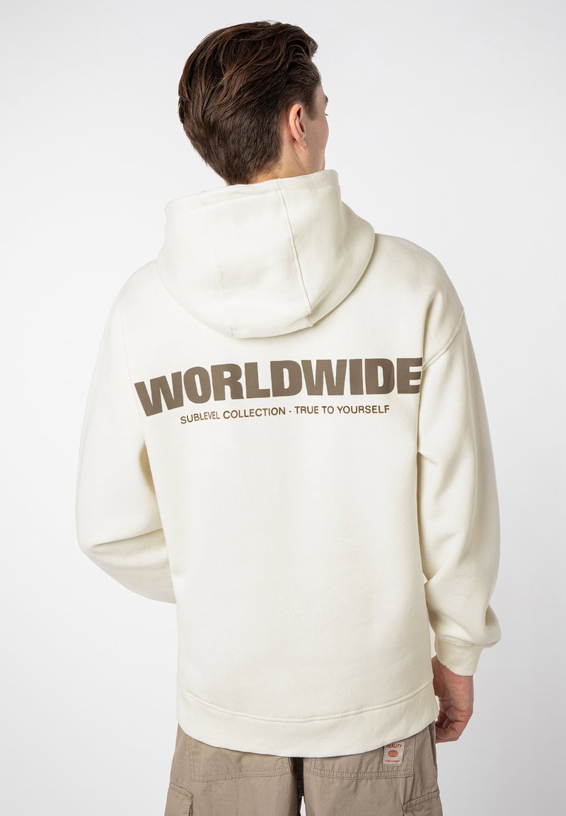 Cremefarbener Hoodie mit einem großen "WORLDWIDE"-Grafik in Braun auf der Rückseite. Mit einer Kapuze mit Kordelzug und gerippten Bündchen. Lässiger Fit.