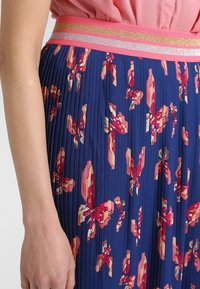 Marinblå klänningstekjol med blommigt mönster i röd och rosa. Har ett brett midjeband i rosa med metalliska randiga detaljer. Slät textur.