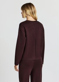 Bordeauxrotes Langarmshirt mit lockerem Schnitt, geripptem Halsausschnitt und einer Rückennaht; aus weichem, strukturiertem Material gefertigt.