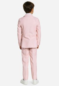 Chaqueta y pantalones de traje en color rosa, combinados con una camisa de vestir blanca, tejido texturizado, silueta ajustada y acompañados de zapatillas blancas.