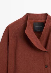 Linnen jas in roestkleur met een sjaalkraag en een zwart merkembleem met de tekst "Massimo Dutti" aan de binnenkant van de halslijn.