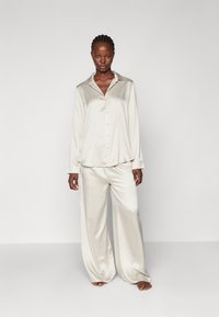 Satin loungewear-set i lys beige, med en langermet skjorte med knapper og brede bukser med en myk, glatt tekstur.